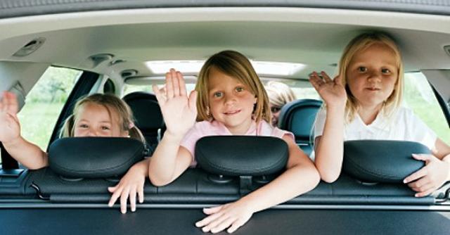 3 little girls waving in the backseat of car