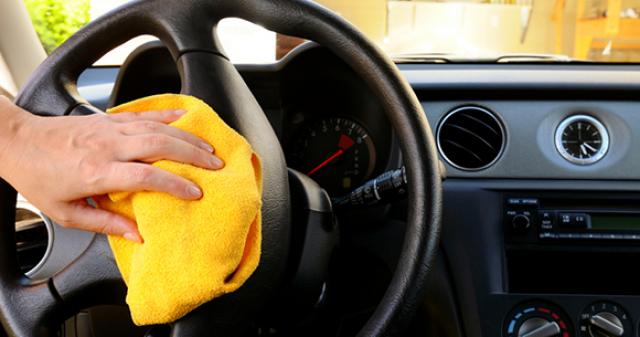 Person cleaning car steering wheel with a yellow towel