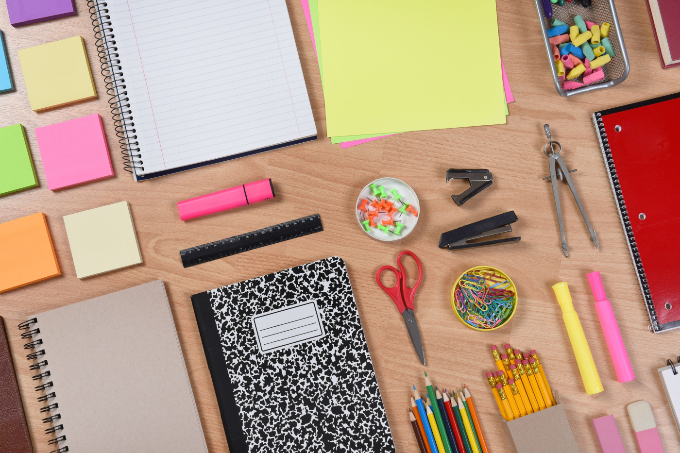 School supplies laid out on a desk including notebooks, scissors, post-its and highlighters