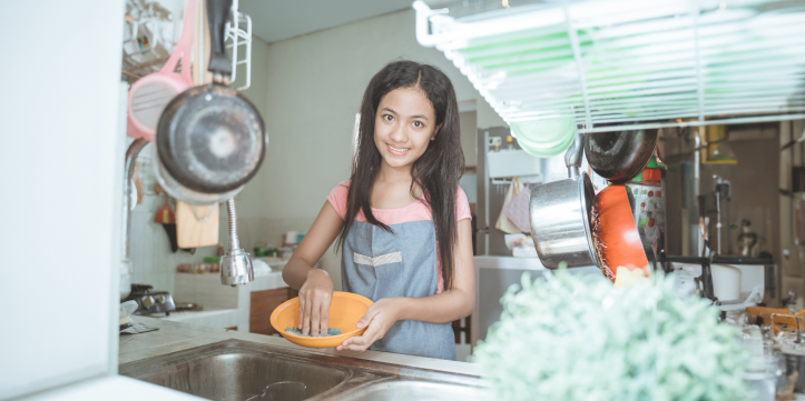 Young girl washing an orange bowl over a sink