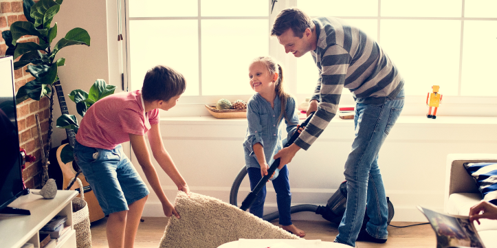 Father and two children, a boy and a girl, vacuuming a rug together